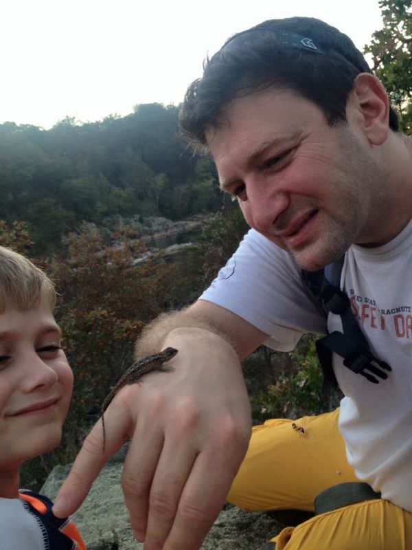 Brian Germain outdoors with one of his sons, showing him a small lizard resting on his hand
